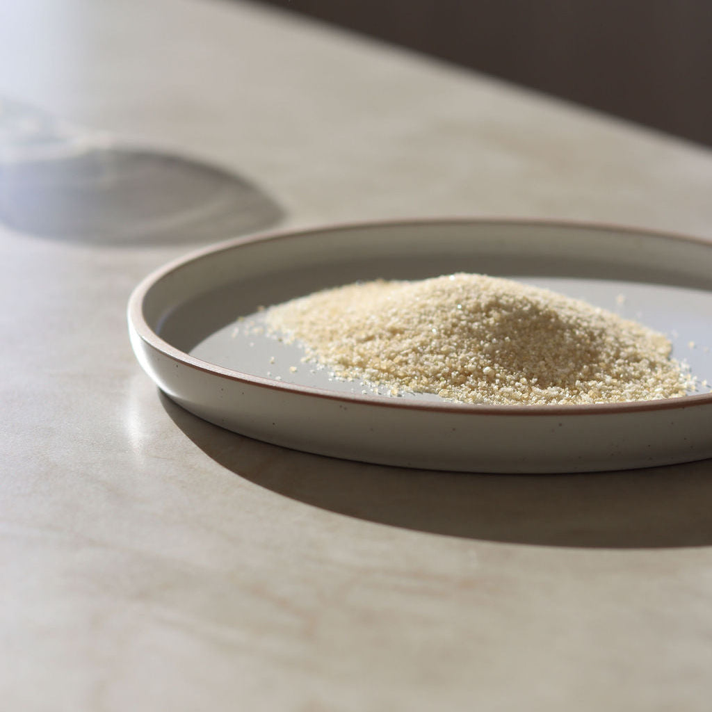A small mound of cocktail rim salts blend, presented on a shallow round ceramic dish resting on a light stone countertop.